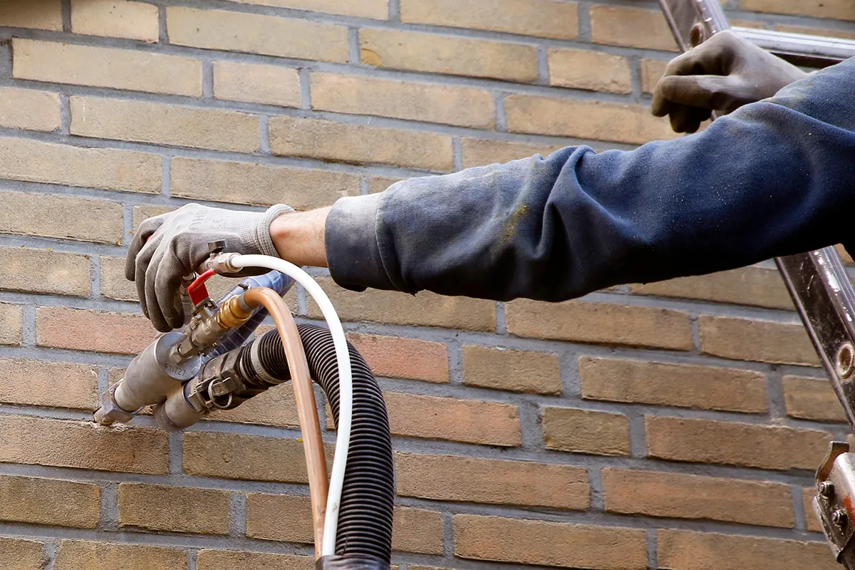 Installateur in rode kleding controleert buitenunit van warmtepomp bij woning in tuin.